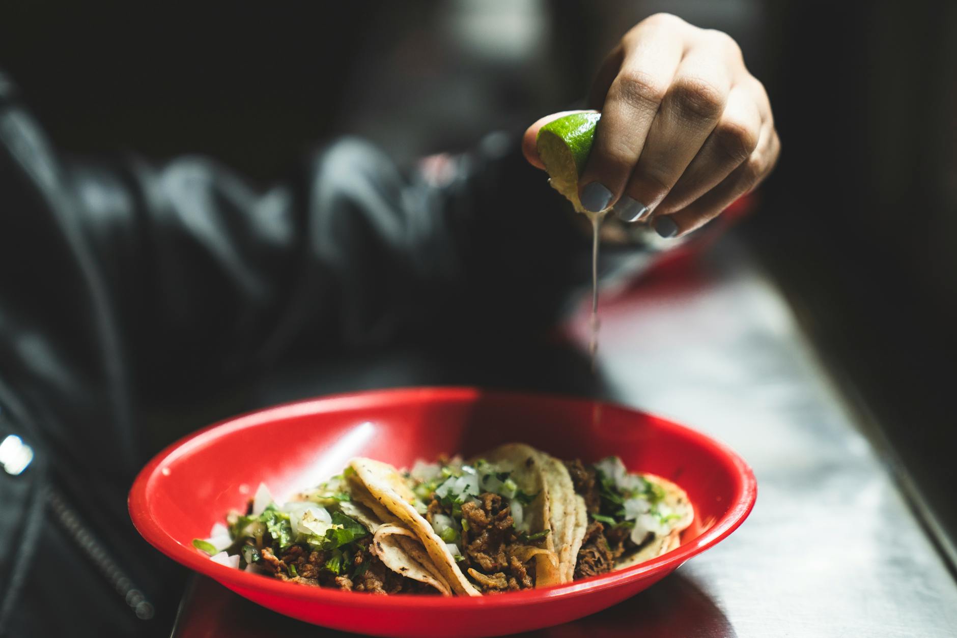 Dłoń wyciskająca limonkę nad meksykańskimi tacos na czerwonym talerzu