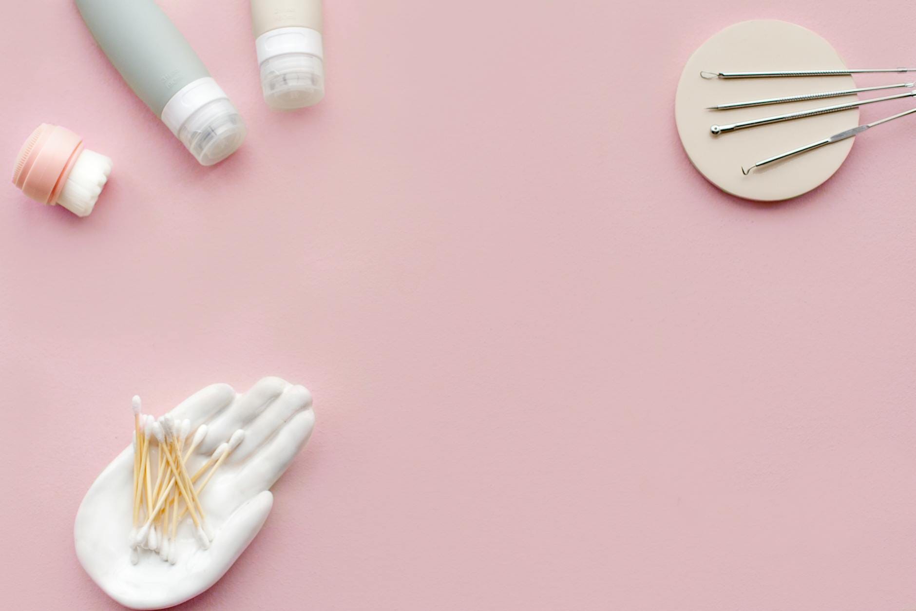 Kosmetyki i akcesoria do pielęgnacji cery ułożone na pastelowym różowym tle