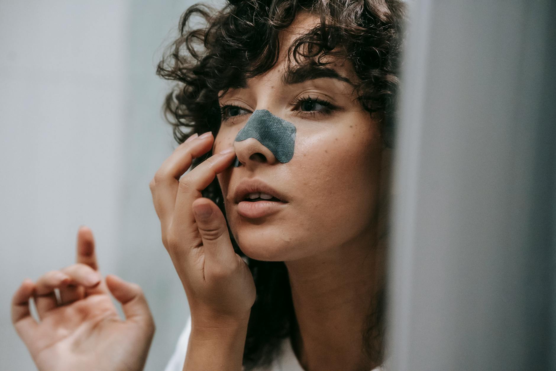Młoda kobieta przykleja plaster na nos przed lustrem w łazience