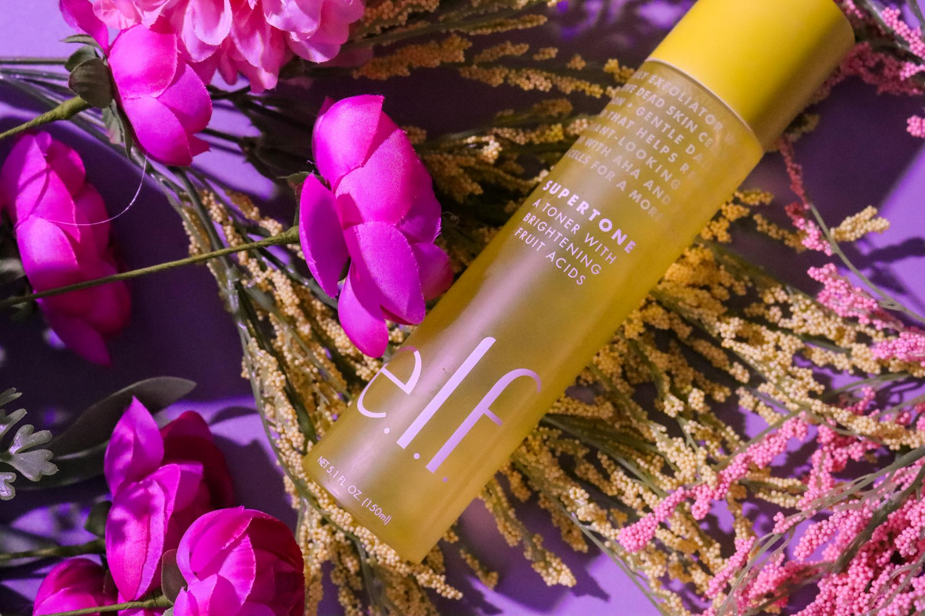 Różowy flakon kosmetyku pielęgnacyjnego w otoczeniu kwiatów i liści