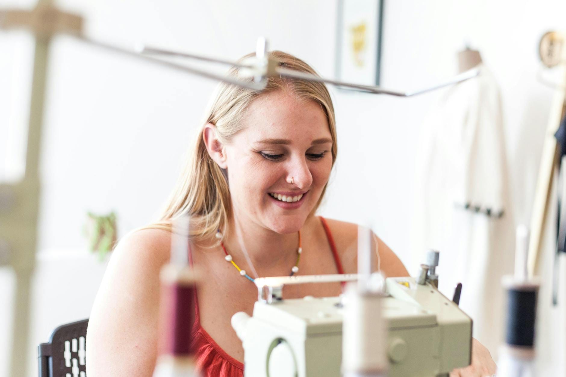 Uśmiechnięta kobieta szyjąca na maszynie w jasnym domowym kąciku