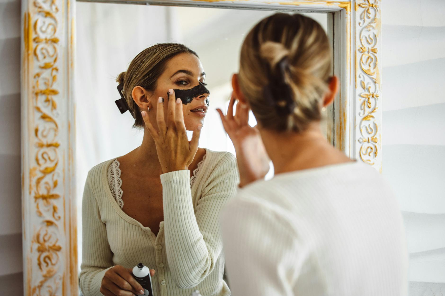 Kobieta nakłada czarną maskę nawilżającą przed lustrem w łazience