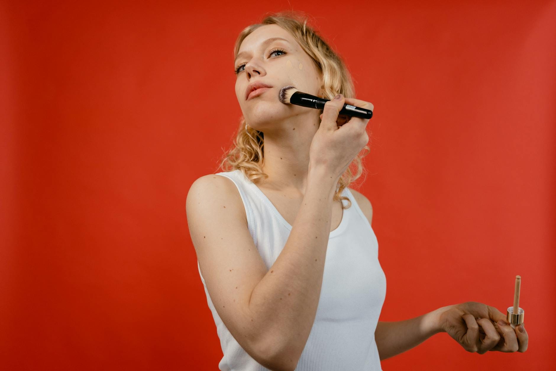 Kobieta nakłada korektor pędzlem na twarz na czerwonym tle