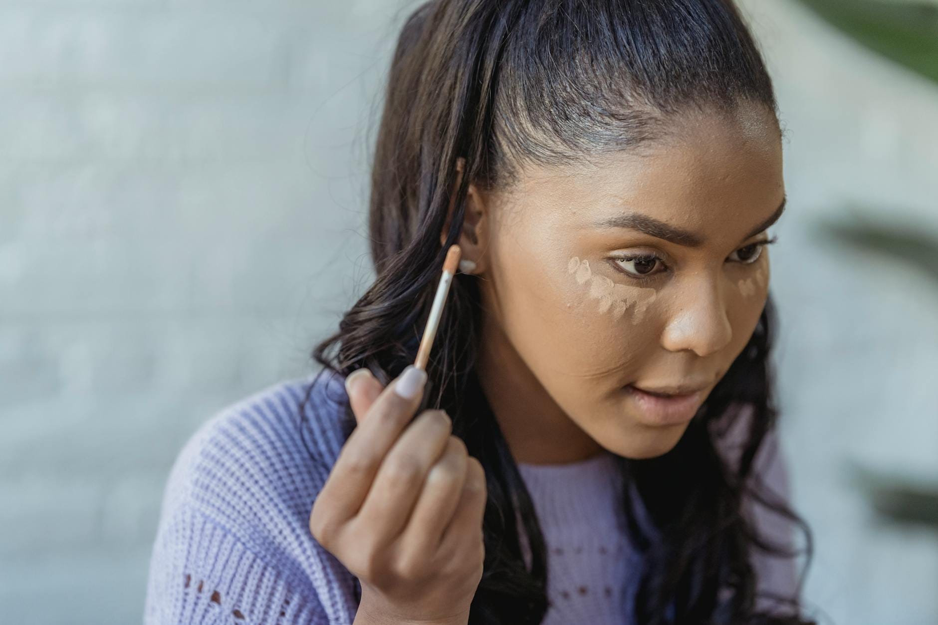 Kobieta o ciemnej cerze nakłada korektor pod oczy w jasnym pokoju