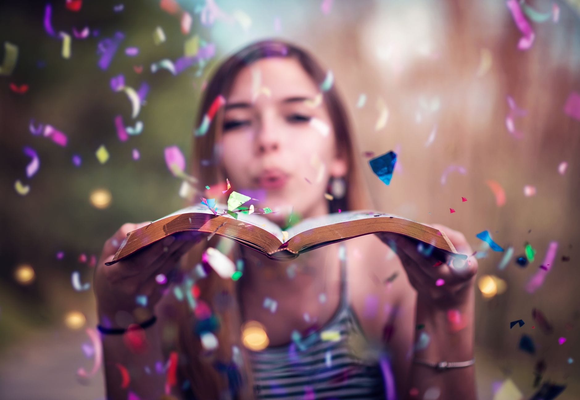 Młoda kobieta dmucha kolorowe konfetti z otwartej książki fantasy