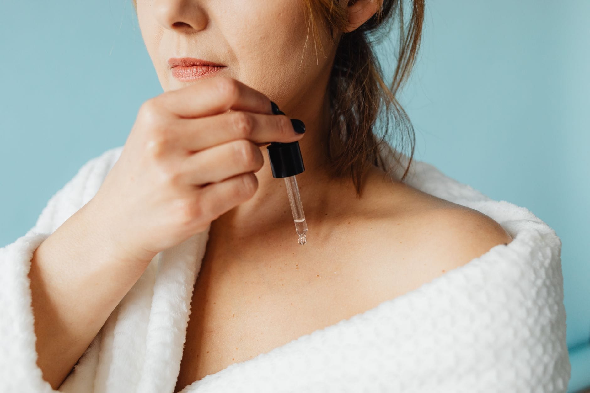 Kobieta w szlafroku nakłada serum na twarz w domowej pielęgnacji